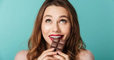 Portrait of a delighted brown haired woman with bright makeup eating chocolate bar