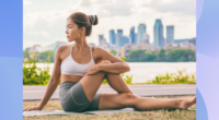 woman in sports bra and biker shorts stretching outdoors on yoga mat in front of city backdrop