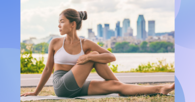 woman in sports bra and biker shorts stretching outdoors on yoga mat in front of city backdrop