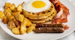 fried egg on waffles seved with homefries, sausages, and bacon