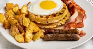 fried egg on waffles seved with homefries, sausages, and bacon