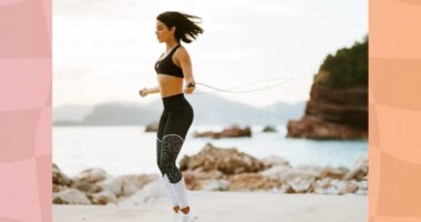 fit brunette woman in black sports bra and black and white leggings doing jump rope workout at the beach