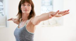 Portrait of mature woman stretching her arms and looking away at gym. Beautiful woman performing yoga in warrior pose, Virabhadrasana.